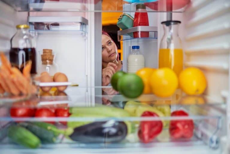 Woman peeking in full refrigerator.